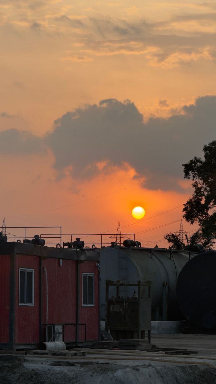 Industrial site with storage tanks at sunset, casting a warm glow in the sky.